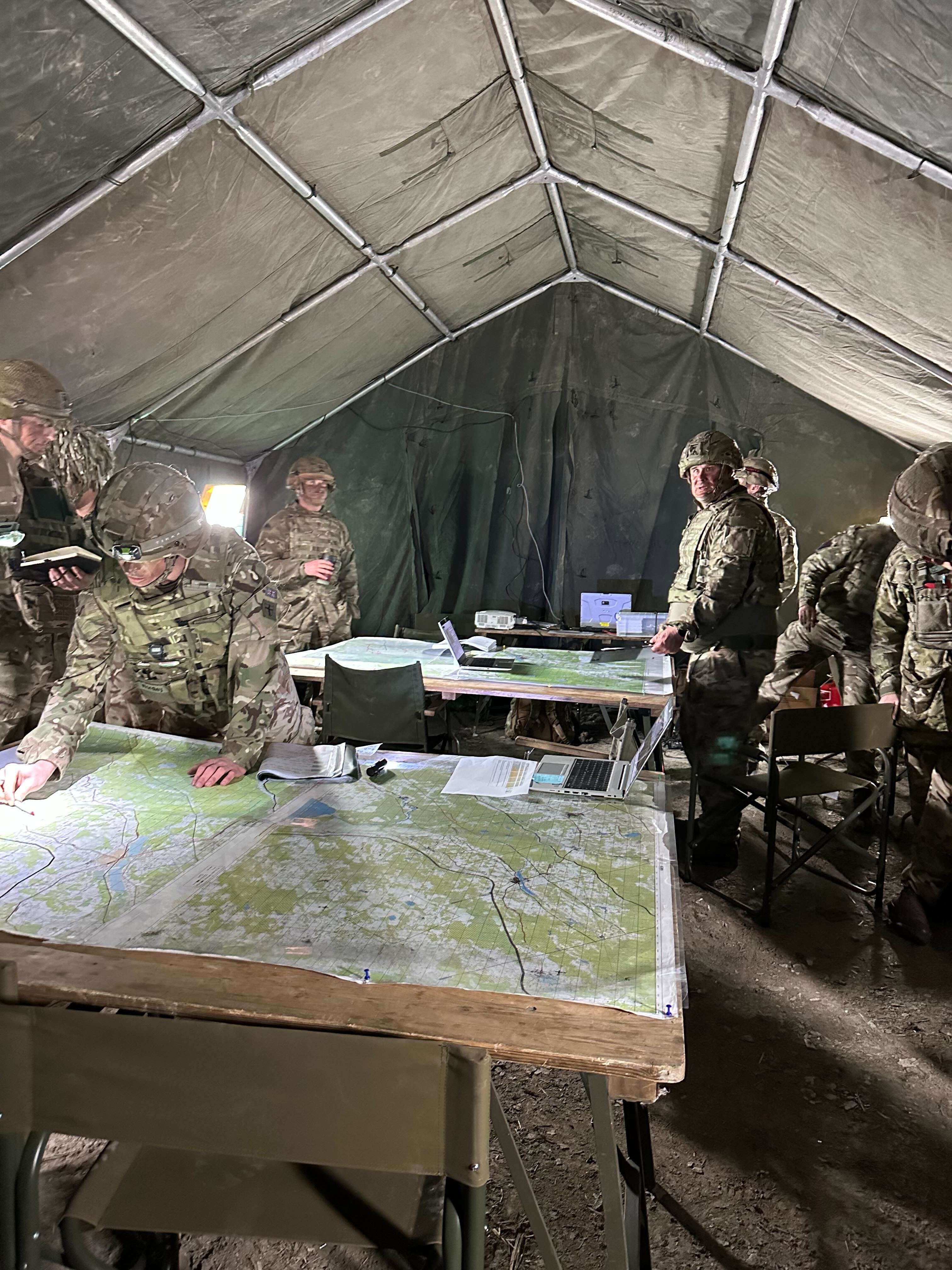 Soldiers in a field command tent planning around map tables